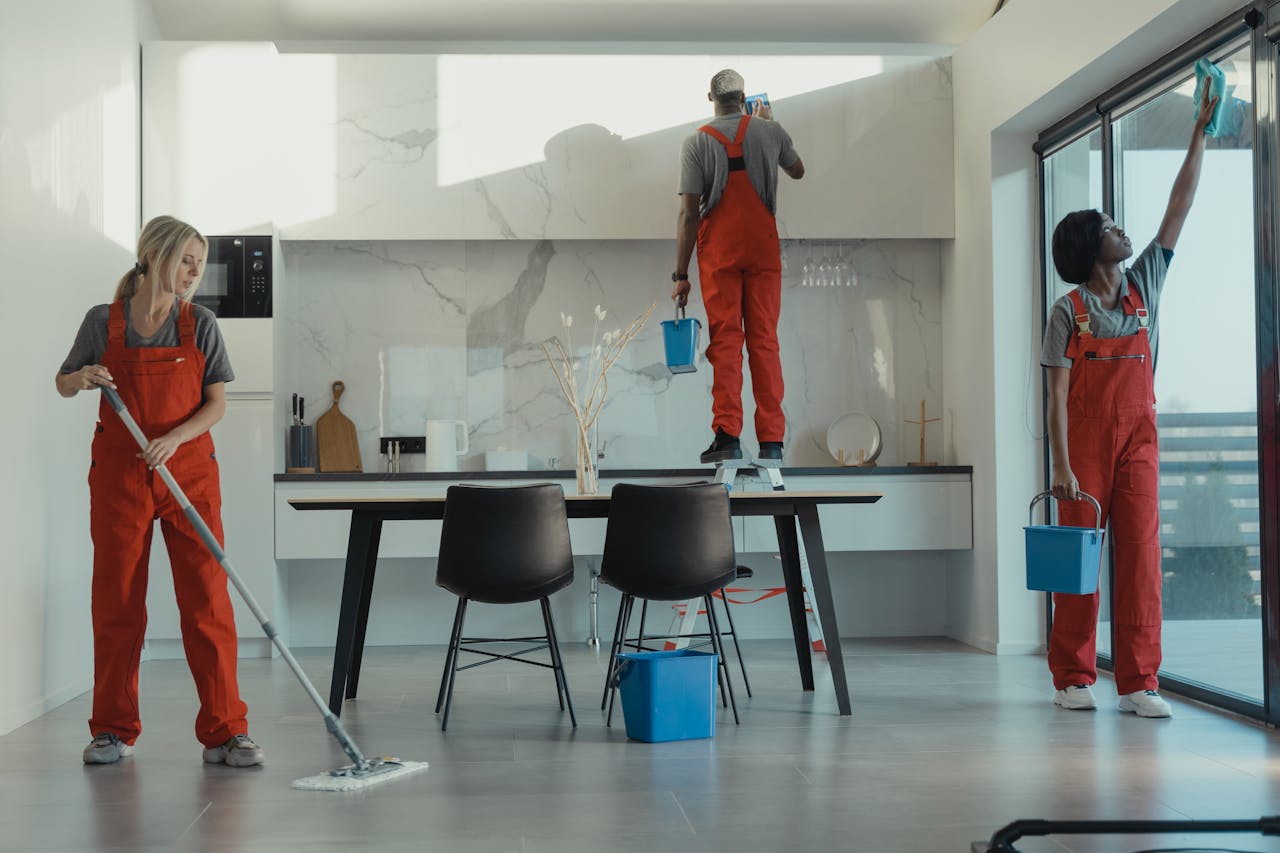 who-we-are Group of cleaners in red uniforms mopping and wiping glass in a modern dining room.