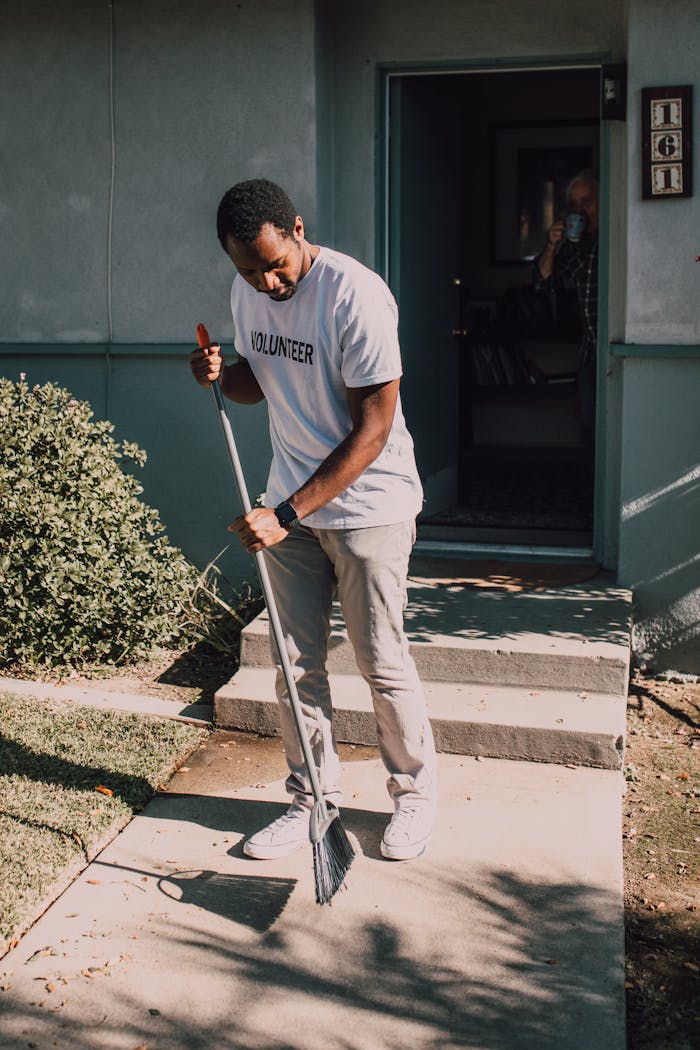 about-us A man in a volunteer shirt sweeping outdoors, showcasing community service.